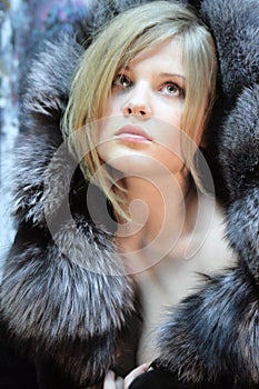 Portrait of a pensive teenage girl, a natural blonde with long hair in a chic silver fox fur coat