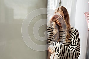 Portrait of pensive thoughtful blond pretty sad, upset, depressed woman sit on window sill, face hands. Covid lockdown