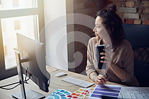 Portrait of pensive woman, interior designer looking aside, drinking coffee or tea while working with color swatches