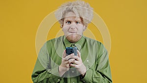 Portrait of pensive young man thinking then texting with smartphone on yellow background