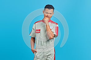 Portrait of pensive young mechanic thinking about question with hand on chin isolated on blue background