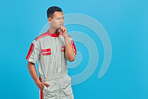 Portrait of pensive young mechanic touching chin with hand and looking sideways isolated on blue background