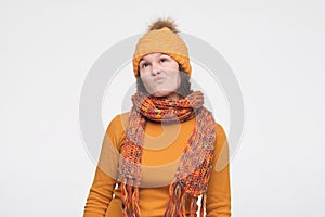 Portrait of pensive young woman in warm scarf and hat looking up