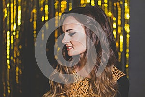 Portrait of perfect young brunette woman with makeup and long wavy brown hair smiling on golden party background