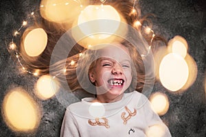 Portrait of a perky laughing 6-year-old girl framed by bokeh from a festive garland. Christmas mood