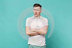 Portrait of perplexed young man in casual clothes standing, holding hands folded isolated on blue turquoise wall