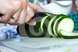 A portrait of a person cutting a zucchini with a sharpp knife in a kitching while cooking a nice and delicious dinner. The