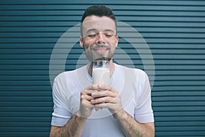 Portrait of person holding glass of milk close to face and enjoying it. He is keeping eues closed. Isolated on striped
