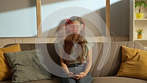 Portrait of person in the room. Woman in headphones looks at smartphone screen, emotionally singing at same time. Double