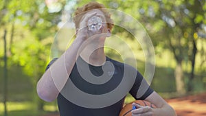 Portrait of perspiring sportsman drinking refreshing water from bottle and looking at camera. Young redhead man posing