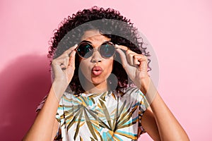 Portrait photo of amazed surprised black skinned curly woman taking off round sunglass isolated on pastel pink color