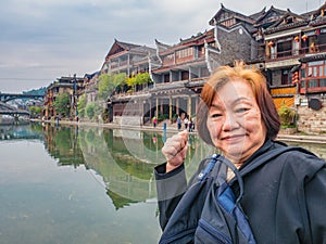 Portrait Photo of asian senior Female backpacker with Scenery view of fenghuang old town