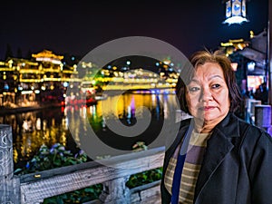 Portrait photo of Asian senior woman with beautiful nightscape of fenghuang old town.