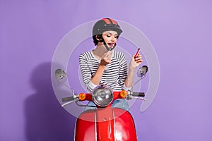 Portrait photo of female motorcycle driver doing make-up applying lipstick lips looking in mirror isolated on bright