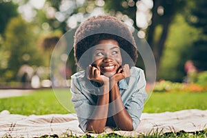 Portrait photo of happy dreamy black skinned female student girl laying on the grass having break in university park