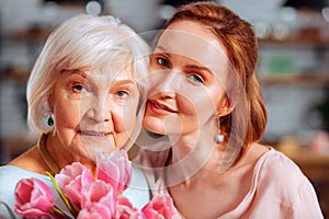 Portrait photo of mature daughter hugging grey-haired mother holding tulips
