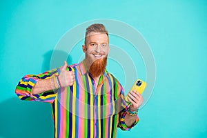 Portrait photo of optimistic red hair beard mustache man has a nice experience rate for new smartphone isolated on cyan