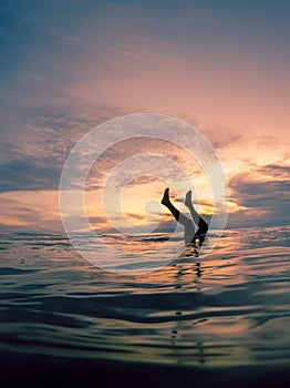 Portrait photograph of a girl doing a handstand in the ocean during sunset