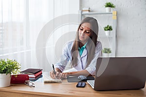 Portrait of physician doctor working in medical office workplace writing prescription sitting at desk.