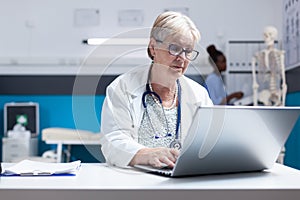 Portrait of physician with stethoscope using laptop to work on healthcare at clinic