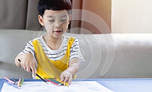 Portrait picture of little kids Asian boy smilling while drawing and coloring in his art book at desk in the living room
