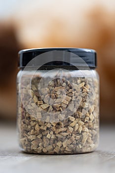 A portrait of a plastic pot or jar full of dried fresh glycyrrhiza glabra liquorice pieces to set a fresh cup of tea. The herbs