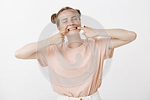 Portrait of playful childish caucasian female student in stylish pink t-shirt with freckles, pulling mouth with fingers