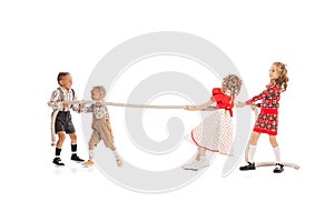 Portrait of playful children, boys and girls pulling the rope isolated over white studio background. opponents