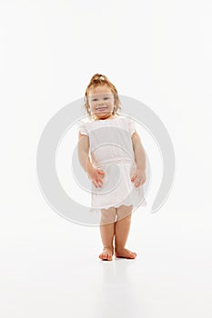 Portrait of playful, cute little girl with wet, curly hair in white dress against white studio background. Baby fashion.