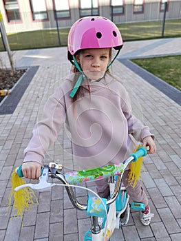 Portrait of a playful funny girl in a pink safety helmet on her bike