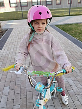 Portrait of a playful funny girl in a pink safety helmet on her bike