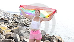 Portrait of a playful girl holding an LGBT flag in her hands on the beach on a sunny day