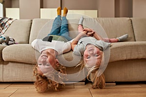 Portrait of playful kids, little boy and girl smiling while lying upside down on a sofa in the living room
