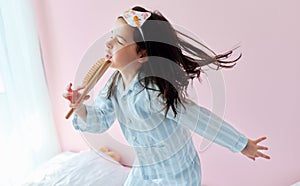 Portrait of a playful little girl in pajama holding a hair brush like microphone singing imitates herself a real singer in the