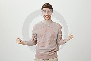 Portrait of playful positive caucasian good-looking man with bristle squeezing fists while being excited and saying yes