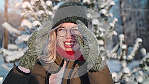 Portrait playful smiling woman hiding face behind mittens having fun at sunny winter forest closeup