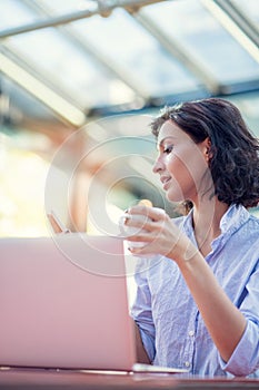 Portrait of a playful young girl taking selfie with mobile phone while sitting with laptop computer at a cafe outdoors