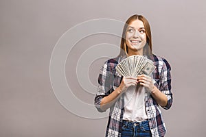 Portrait of a playful young woman with long hair holding bunch of money banknotes and looking away at copy space isolated over