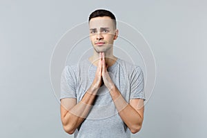 Portrait of pleading young man in casual clothes looking camera, folded his hands, praying isolated on grey wall