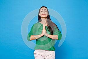 Portrait of pleading young woman in green casual clothes looking camera, holding hands folded in prayer isolated on