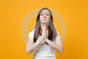 Portrait of pleading young woman in white casual clothes looking camera, holding hands folded, praying  on