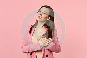 Portrait of pleasant beautiful young woman in jacket keeping hands on chest, heart  on pastel pink wall