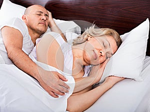 Portrait of pleasant mature couple napping in bed