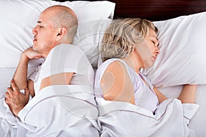 Portrait of pleasant ordinary mature couple napping in bed