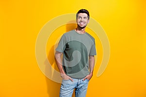 Portrait of pleasant positive guy wear stylish t-shirt plams in pockets look at promo empty space isolated on yellow