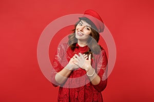 Portrait of pleasant smiling young woman in lace dress cap holding hands crossed on heart, chest isolated on bright red