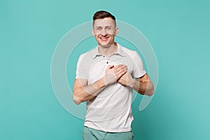 Portrait of pleasant young man in casual clothes standing holding hands on heart, chest isolated on blue turquoise