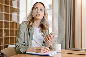 Portrait of pleased blond woman writing down notes