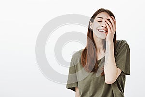 Portrait of pleased confident good-looking urban female in dark-green t-shirt, holding palm on face and smiling broadly