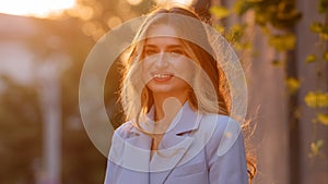 Portrait pleased happy Caucasian blonde girl with long hair stands sun rays background looking at camera smiling